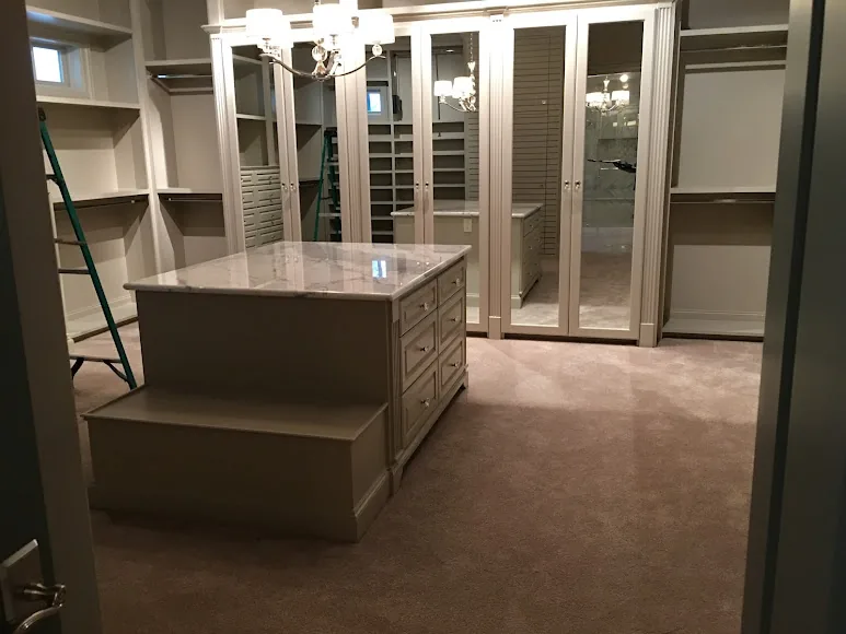 RM dressing room with storage island, mirrored doors and surrounding shelves.